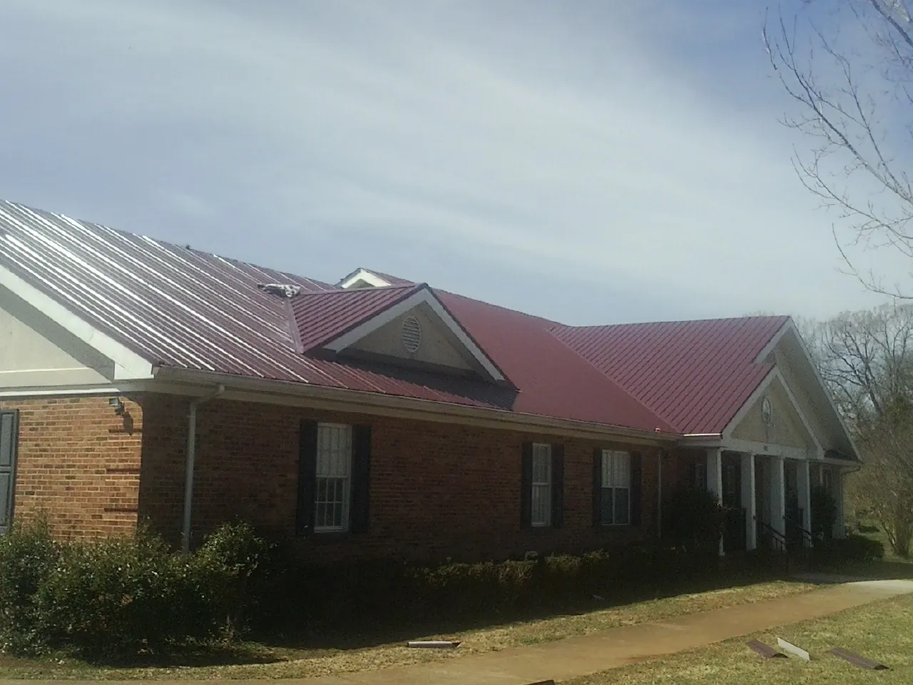 Red metal roof with gabled entries on a long brick building, from a Hail Damage Roof Repair job in Rindge