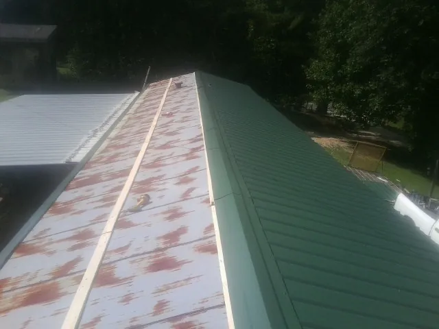 Old rusted panels beside newly installed green metal roofing — Wind Damage Roof Repair by Roofing Brothers in Rindge
