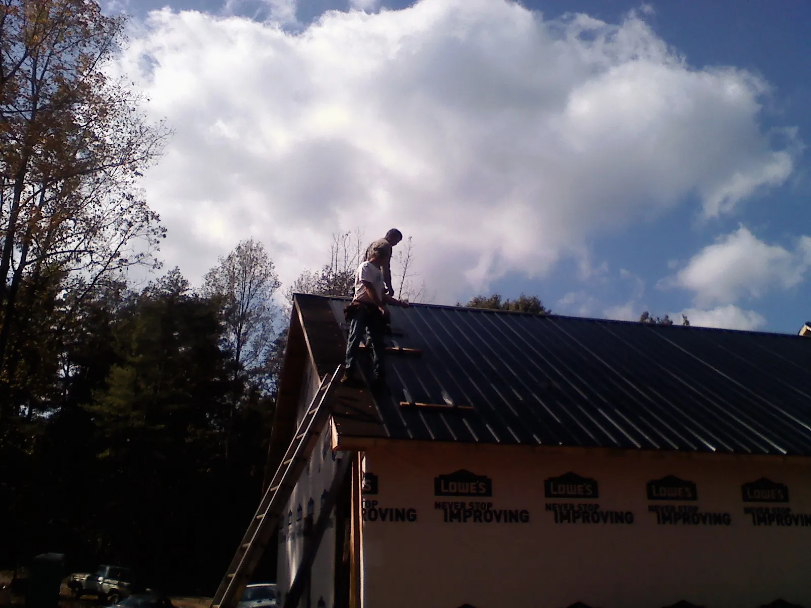 Roofer fastening dark metal panels high against a cloudy sky, from a Roof Inspection job in Rindge