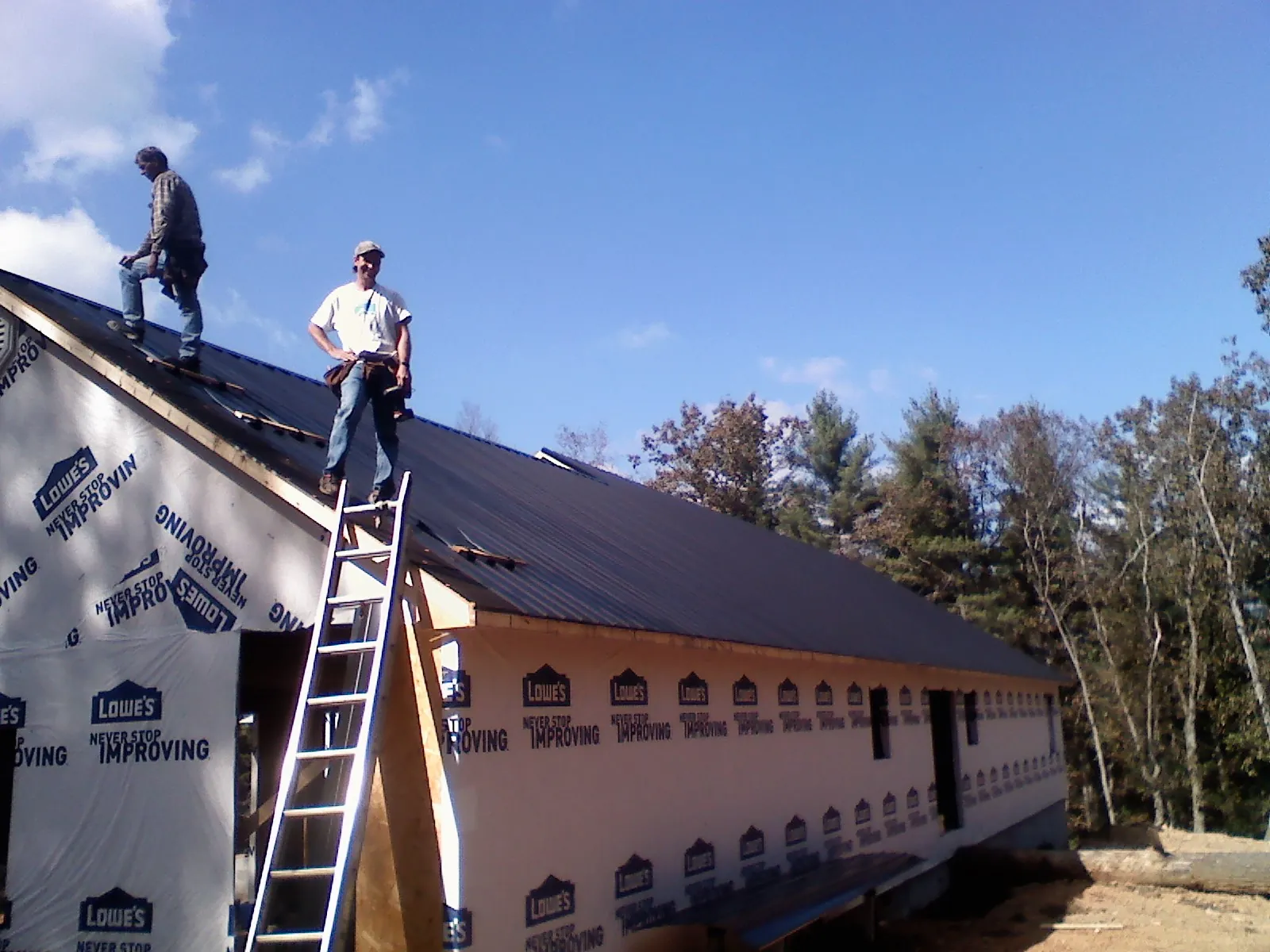 Two roofers standing on a long dark metal roof over a wrapped building in Rindge