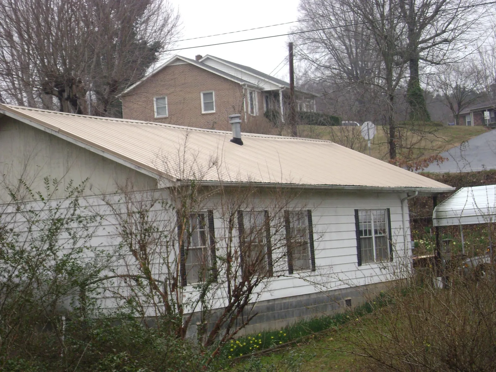 Tan metal roof on a white sided house set into a hillside — Commercial Roofing by Roofing Brothers in Rindge